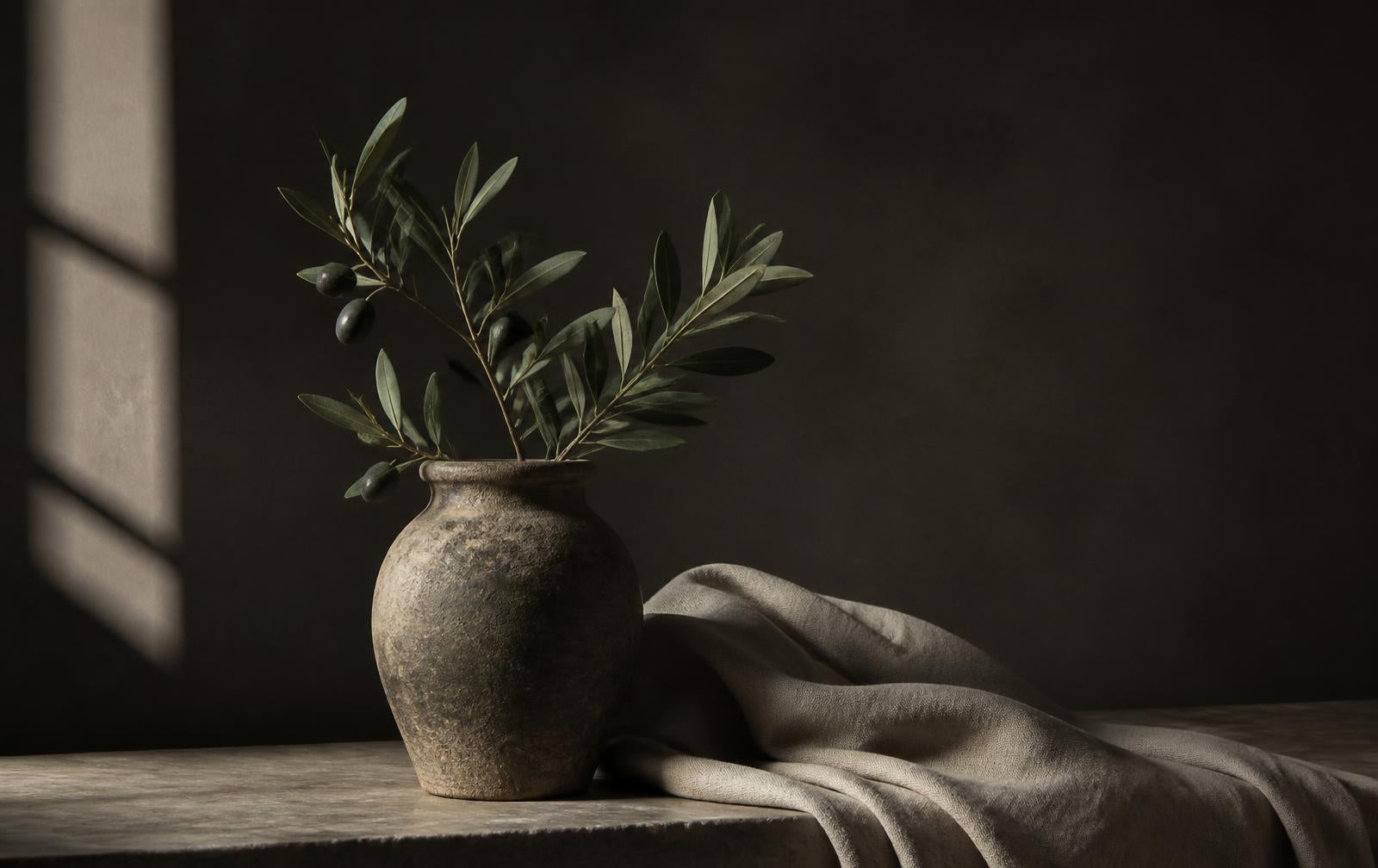Stone vase with olive branch beside draped linen