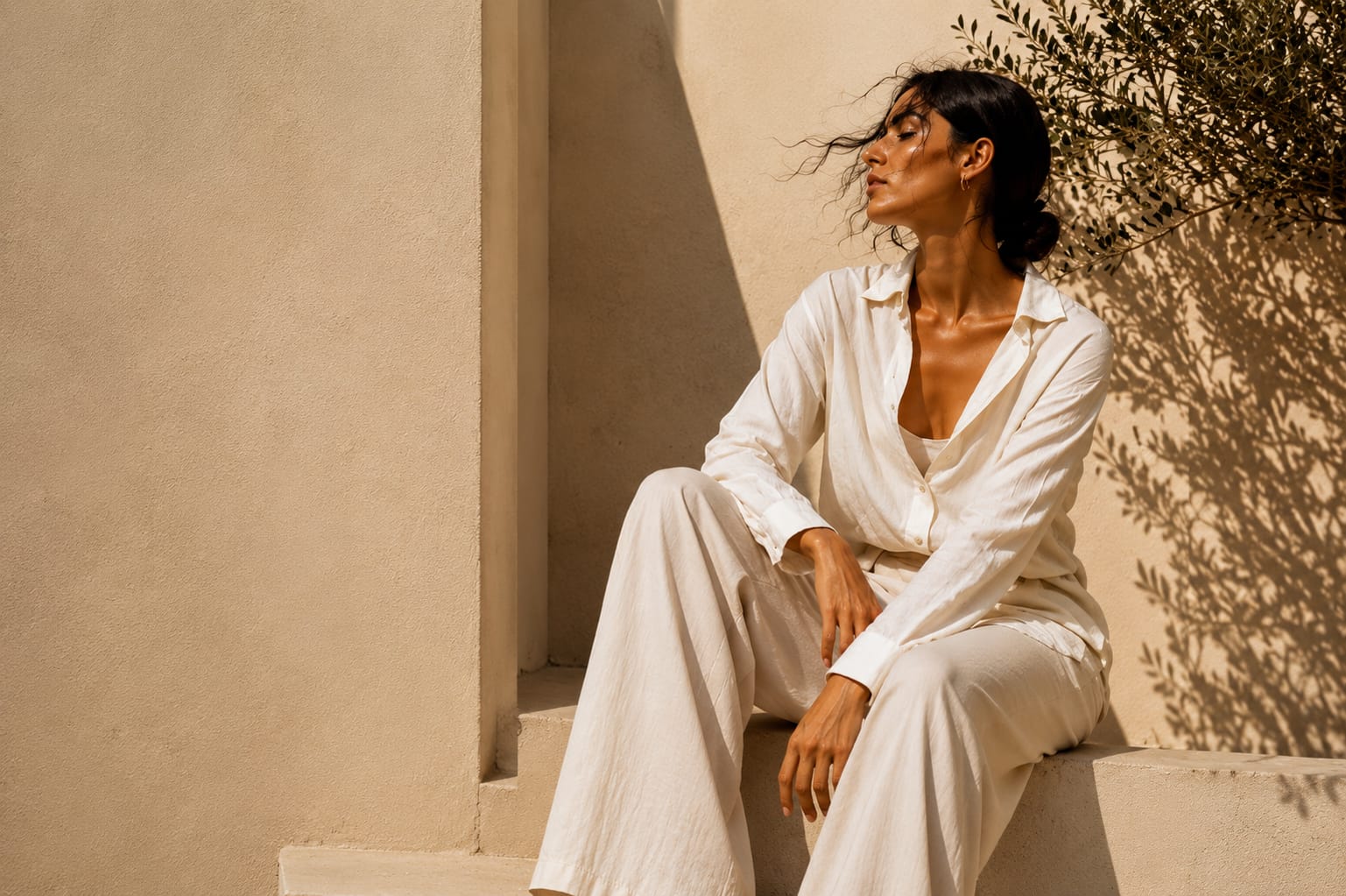 Model in washed ivory linen against a sunlit Mediterranean wall